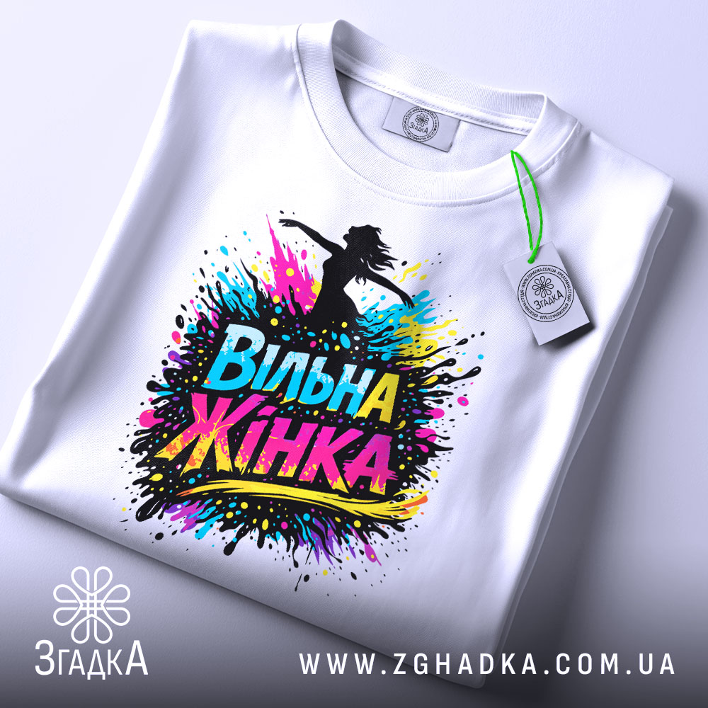 Футболка вільна жінка, білого кольору, зображена зверху, на столі, фон світло-блакитний, принт з написом 'Вільна Жінка' у яскравих кольорах, з етикеткою на комірці.