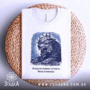 Футболка влада і сутність, білого кольору, складена на плетеній кошику, фон білий, принт з малюнком лева з короною в темно-синіх тонах, текст під малюнком.