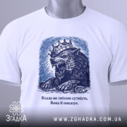 Футболка влада і сутність, білого кольору, зображена зверху, фон світло-сірий, принт з малюнком лева з короною в темно-синіх тонах, текст під малюнком, на футболці є етикетка з зеленим шнурком.