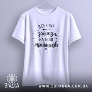 Футболка всесвіт на боці, біла, підвішена на вішалці, фон світло-сірий, принт чорний з написом 'всесвіт завжди на боці мрійників' та декоративними зірочками.