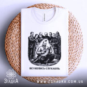 Футболка всі колись слухають, білого кольору, складена на плетеній кошику, фон світло-сірий, принт чорного кольору з зображенням чоловіка, що грає на бандурі, оточеного групою людей.