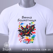 Футболка винна бешкетниця, білого кольору, складена на поверхні, фон світлий, принт з чорним котом, червоним вином та яскравими кольоровими акцентами, на футболці є етикетка.