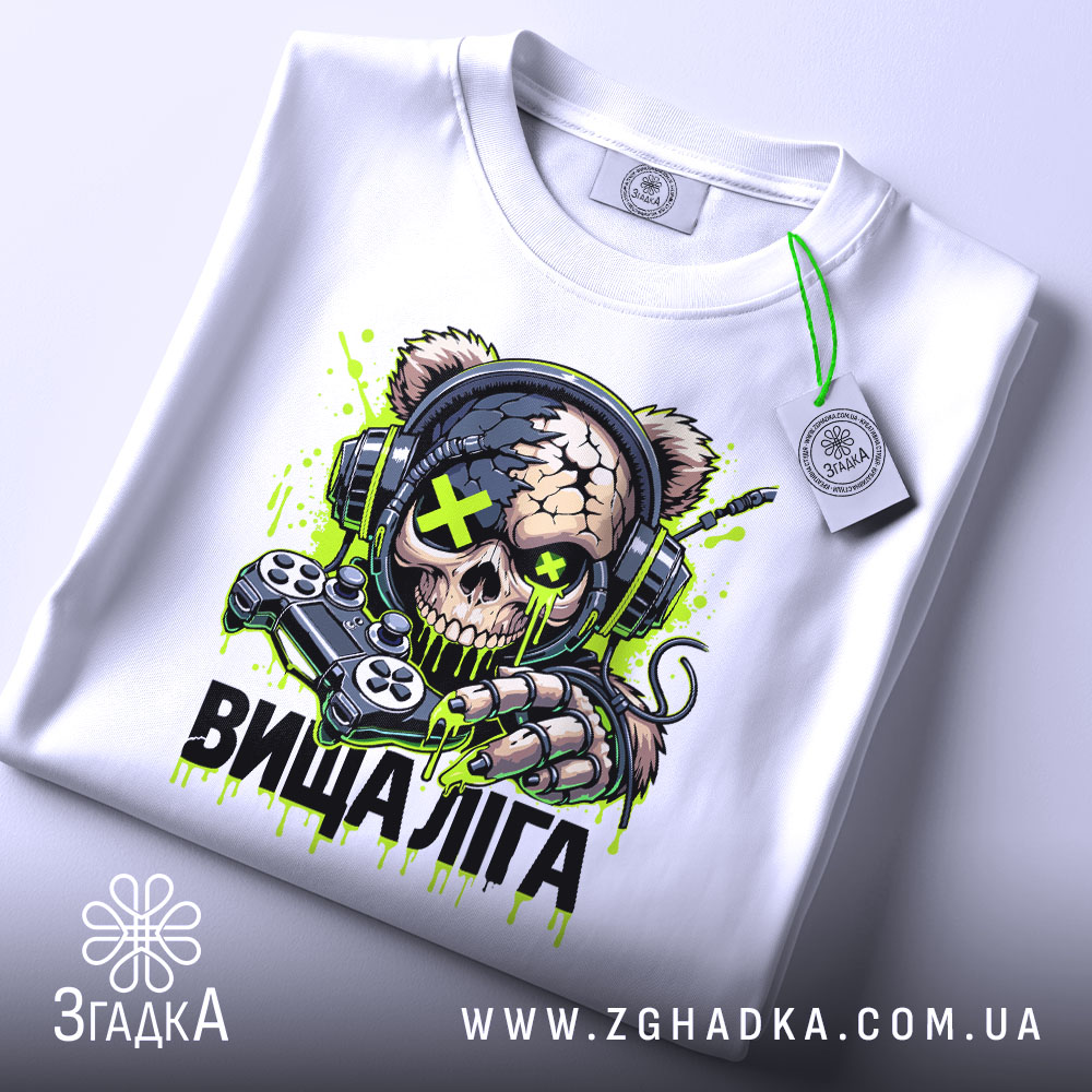 Футболка вища ліга. Біла футболка, розкладена на поверхні, з яскравим принтом черепоподібної ведмедиці в навушниках, що тримає геймпад. Принт має зелені та чорні деталі, а на футболці висить етикетка. Фон світлий.
