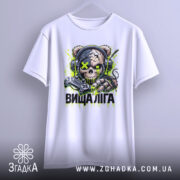 Футболка вища ліга. Біла футболка, підвішена на вішалці, з принтом черепоподібної ведмедиці в навушниках, що тримає геймпад. Принт яскравий, з зеленими та чорними акцентами, фон світлий і нейтральний.