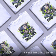 Футболка вища ліга. Біла футболка з яскравим принтом, на якому зображена черепоподібна ведмедиця в навушниках, що тримає геймпад. Принт виконаний у зелених і чорних кольорах, фон світлий, а футболка представлена на манекені з правого ракурсу.