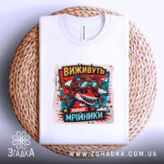 Футболка виживуть лише мрійники. Біла футболка, складена на плетеному кошику, з принтом червоного вовка в окулярах та шоломі, оточеного кольоровими зірками. Фон світло-сірий, що підкреслює текстуру кошика.