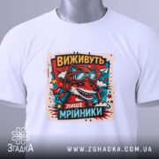 Футболка виживуть лише мрійники. Біла футболка, складена на столі, з принтом червоного вовка в окулярах та шоломі, оточеного кольоровими зірками. На футболці є етикетка з зеленим шнурком. Фон світло-сірий.