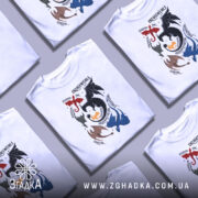 Футболка з драконячою тематикою — кілька складених футболок, композиція на столі.