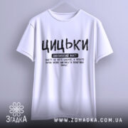 Футболка з написом цицьки, білого кольору, підвішена на вішалці з нейтральним фоном, принт чорного кольору з великими буквами, текст розташований по центру.