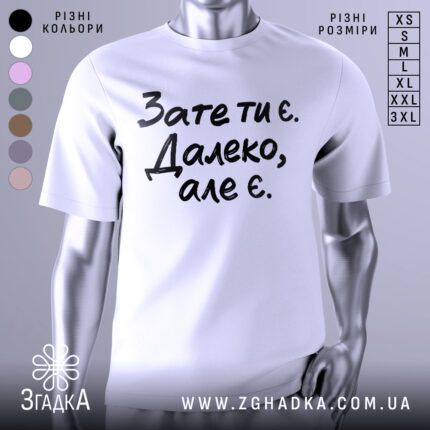 Футболка зате ти є. Білий колір, зображена з фронтального ракурсу на манекені, фон нейтральний, принт чорного кольору з текстом 'Зате ти є. Далеко, але є.'