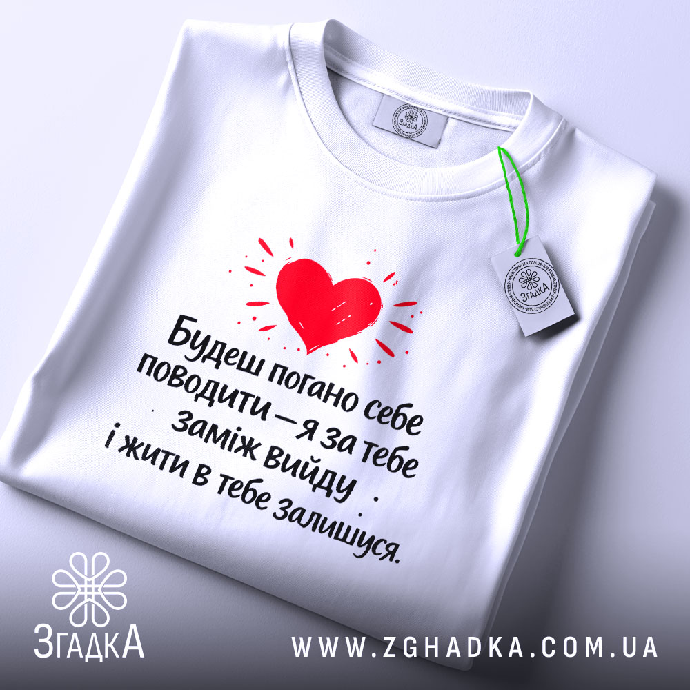 Футболка жарт про шлюб, біла, зображена зверху, фон світлий, принт червоного серця з текстом чорного кольору, на комірці є етикетка.