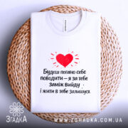 Футболка жарт про шлюб, біла, зображена на плетеній кошику, фон нейтральний, принт червоного серця з текстом чорного кольору.