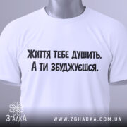 Футболка життєвий тиск, біла, складена на поверхні, фон світло-сірий, принт чорного кольору з текстом 'Життя тебе душить. А ти збуджуєшся.', на комірці видна етикетка.