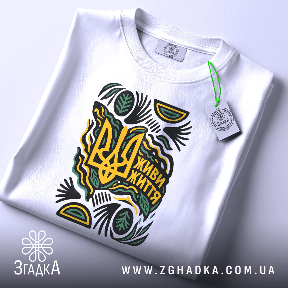 Футболка живи життя білого кольору, складена на поверхні, з принтом у вигляді тризуба та написом 'Живи життя', прикрашена зеленими та жовтими елементами, з етикеткою, що звисає з коміра.