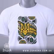 Футболка живи життя білого кольору, складена на поверхні, з принтом у вигляді тризуба та написом 'Живи життя', прикрашена зеленими та жовтими елементами, з етикеткою, що звисає з коміра.