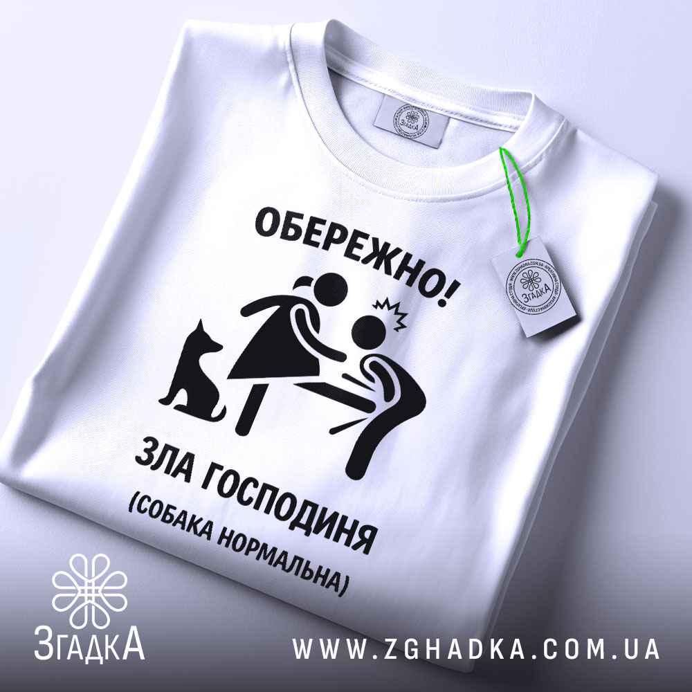 Футболка зла господиня, біла, зображена зверху, фон світлий, принт чорного кольору з малюнком жінки та чоловіка, а також чорна собака, на футболці є етикетка з зеленим шнурком.
