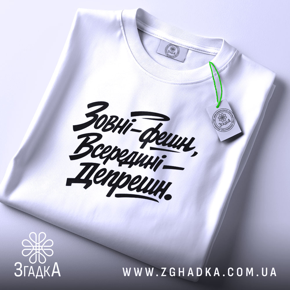 Футболка зовні фешн, біла, складена на поверхні, з видимим етикеткою, фон світло-сірий, принт чорний з текстом 'Зовні-фешн, Всередині—Депрешн.'