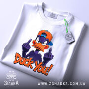Футболка зухвалий качур, білого кольору, зображена на столі, фон світло-сірий, принт з качуром у кепці, який показує два середніх пальці, текст 'Duck You!' яскравого оранжевого кольору, на футболці є етикетка.