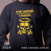 Світшот Я не святий. Чорний колір, близький ракурс на верхню частину, фон з розмитим градієнтом. Принт з жовтим черепом та написом, кругла горловина, фактура м'яка, манжети з еластичного трикотажу.