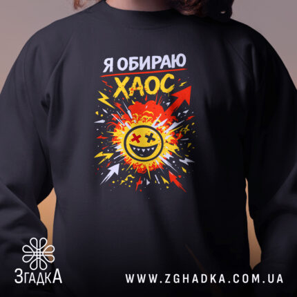 Світшот Я обираю хаос, чорний колір, близький ракурс, фон з розмитим освітленням, яскравий принт з усміхненим обличчям на фоні вибуху, кругла горловина, манжети на рукавах, фактура м'яка та комфортна.