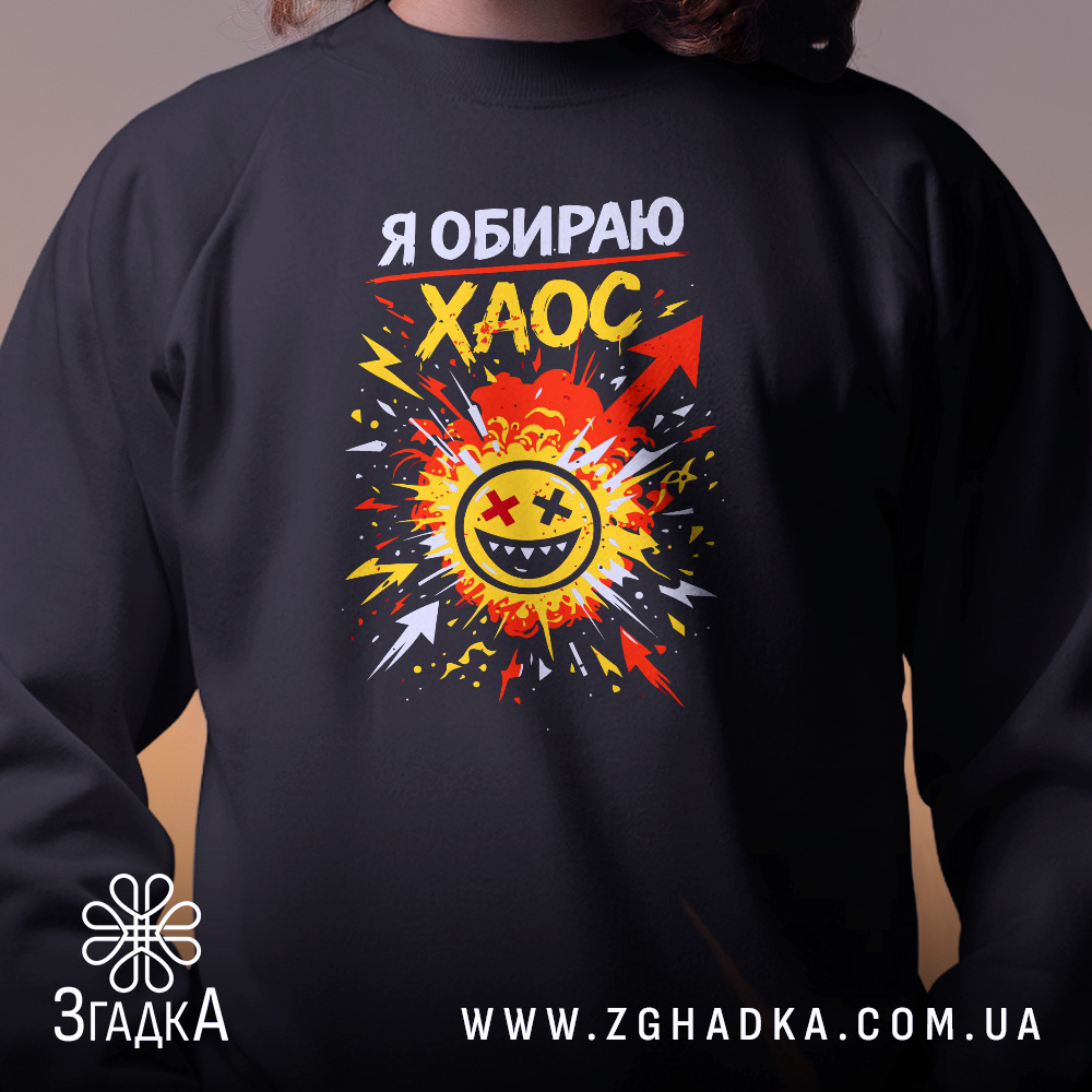 Світшот Я обираю хаос, чорний колір, близький ракурс, фон з розмитим освітленням, яскравий принт з усміхненим обличчям на фоні вибуху, кругла горловина, манжети на рукавах, фактура м'яка та комфортна.