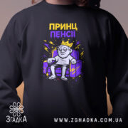 Світшот Принц пенсії, чорного кольору, зображений на людині, ракурс з близької відстані, фон розмитий, деталі принта з персонажем у короні на дивані, кругла горловина, манжети з трикотажної резинки, фактура м'яка та комфортна.