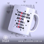 Чашка для бабусі. Чаша білого кольору, з написом, що складається з чорних і червоних букв, розташованим на передньому плані. Ручка класичної форми, край рівний, поверхня глянцева. Фон світло-сірий з сердечками.