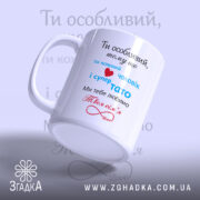 Чашка для коханого чоловіка, біла з кольоровим принтом, зображена з лівого ракурсу, на фоні світло-блакитного градієнта. Принт містить текст червоного, синього та чорного кольорів, ручка округлої форми, край рівний, поверхня глянцева.