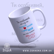 Чашка для коханого чоловіка, біла з кольоровим принтом, зображена з правого ракурсу, на фоні світло-блакитного градієнта. Принт містить текст червоного, синього та чорного кольорів, ручка округлої форми, край рівний, поверхня глянцева.