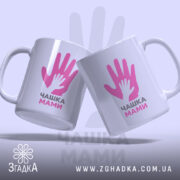 Чашка для мами, дві білих чашки, з ракурсом спереду, на фоні світло-фіолетового кольору, з принтом у вигляді двох рук, напис "ЧАШКА МАМИ" чорним шрифтом, ручки круглі, краї рівні, глянцеві.