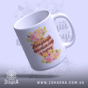 Чашка для найкращого вихователя, біла з квітковим дизайном, напис 'Найкращий вихователь у садочку' на видимій стороні, ручка стандартна, край рівний, глянець на поверхні.