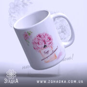 Чашка для подарунку на свято, біла з яскравим принтом, зображення квітів і написом "Будь найщасливішою!", ручка класична, край рівний, глянцеве покриття, фон світлий з легким малюнком квітів.