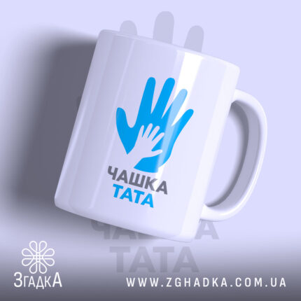Чашка для тата, біла, зображена з легким нахилом, на фоні світло-фіолетового кольору, з принтом у вигляді рук блакитного кольору та написом 'ЧАШКА ТАТА' чорного кольору, ручка округлої форми, край рівний, глянцева поверхня.