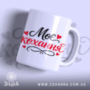 Чашка Моє кохання, біла з чорним і червоним написом "Моє кохання" та сердечками, з гладкою поверхнею, ручка з класичним вигином, край рівний, матова текстура.