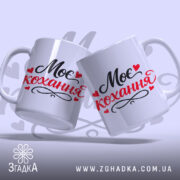 Чашка Моє кохання, дві чашки, обидві білі з чорним і червоним написом "Моє кохання" та сердечками, з гладкою поверхнею, ручки класичної форми, краї рівні, матова текстура.
