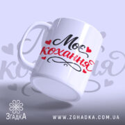 Чашка Моє кохання, біла з чорним і червоним написом "Моє кохання" та сердечками, з гладкою поверхнею, ручка з класичним вигином, край рівний, матова текстура.