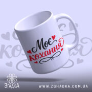 Чашка Моє кохання, біла з чорним і червоним написом "Моє кохання" та сердечками, з гладкою поверхнею, ручка з класичним вигином, край рівний, матова текстура.