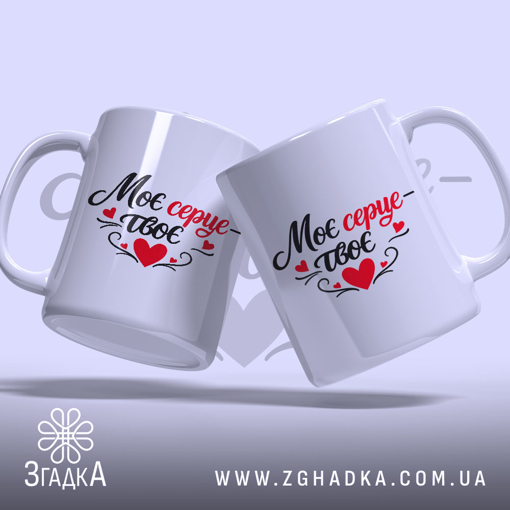 Чашка Моє серце – твоє, дві білих чашки з легким глянцем, розташовані під кутом, з написом чорного та червоного кольорів, ручки традиційної форми, фон ніжно-фіолетовий, на задньому плані розмитий текст.