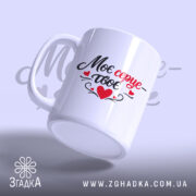 Чашка Моє серце – твоє, біла, з легким глянцем, з написом чорного та червоного кольорів, ручка з традиційним дизайном, край рівний, фон ніжно-фіолетовий, на задньому плані розмитий текст.