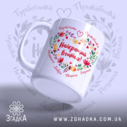 Чашка Найкращий Вчитель, біла з кольоровим принтом, показана з лівого боку, на фоні світло-фіолетового кольору, з написом "Найкращий вчитель!" в центрі, оточеним квітами і сердечками, ручка класична, край рівний, глянцевий.