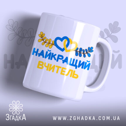 Чашка патріотична для вчителя, біла, з написом 'НАЙКРАЩИЙ ВЧИТЕЛЬ' жовтого та синього кольорів, оформлена зображенням сердець та листя, ручка округлої форми, край гладкий, глянцева поверхня, фон світло-фіолетовий.