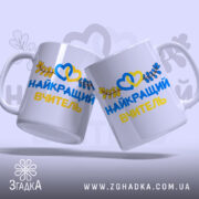 Чашка патріотична для вчителя, дві однакові чашки, біла, з написом 'НАЙКРАЩИЙ ВЧИТЕЛЬ' жовтого та синього кольорів, оформлена зображенням сердець та листя, ручки округлої форми, край гладкий, глянцева поверхня, фон світло-фіолетовий.
