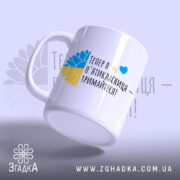 Чашка привітання найкращому вчителю, біла з кольоровим принтом, зображення соняшника в жовто-блакитних кольорах, напис чорним шрифтом, ручка класична, край рівний, глянцеве покриття, чашка нахилена.