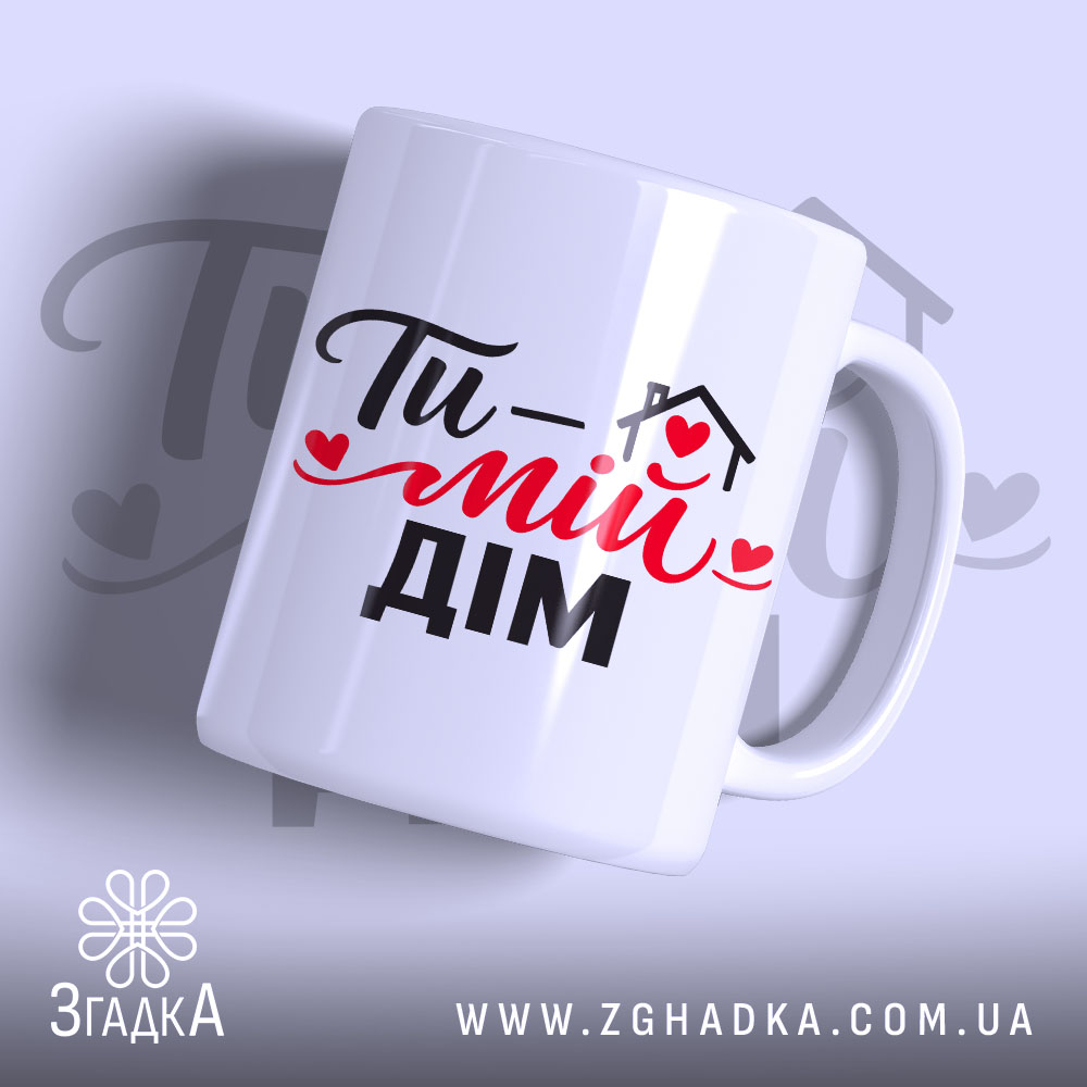 Чашка Ти – мій дім, біла з чорним і червоним принтом, з написом 'Ти – мій дім', ручка з класичним дизайном, край рівний, матова поверхня, фон світло-фіолетовий.