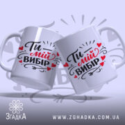 Чашка Ти – мій вибір, дві білі чашки з однаковим принтом, показані під кутом на світло-сірому фоні, з написом "Ти – мій вибір" в чорному і червоному кольорах, обидві чашки мають гладкі ручки та рівні краї, з глянцевою поверхнею.