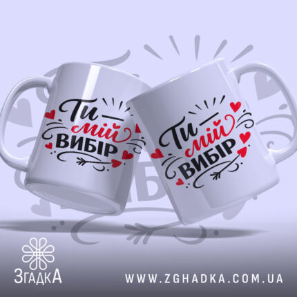 Чашка Ти – мій вибір, дві білі чашки з однаковим принтом, показані під кутом на світло-сірому фоні, з написом "Ти – мій вибір" в чорному і червоному кольорах, обидві чашки мають гладкі ручки та рівні краї, з глянцевою поверхнею.
