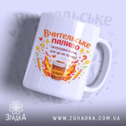 Чашка вчителю на подарунок, біла, з фронтального ракурсу, на світло-синьому фоні, з яскравим принтом, що містить напис 'Вчительське паливо' та малюнок чашки з кавою, ручка округлої форми, край рівний, глянцевий.
