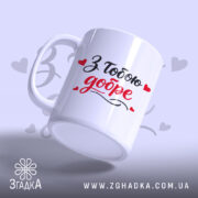 Чашка З тобою добре, біла, з написом "З тобою добре" в чорному та червоному кольорах, ручка гладка, край рівний, матова поверхня, фон ніжно-фіолетовий з сердечками.