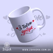 Чашка З тобою добре, біла, з написом "З тобою добре" в червоному та чорному кольорах, ручка гладка, край рівний, матова поверхня, фон ніжно-фіолетовий з сердечками.