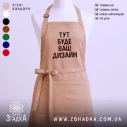 Фартух з вашим дизайном, бежевого кольору, зображений з фронтального ракурсу на манекені, фон світлий, принт чорного кольору з текстом 'ТУТ БУДЕ ВАШ ДИЗАЙН'.